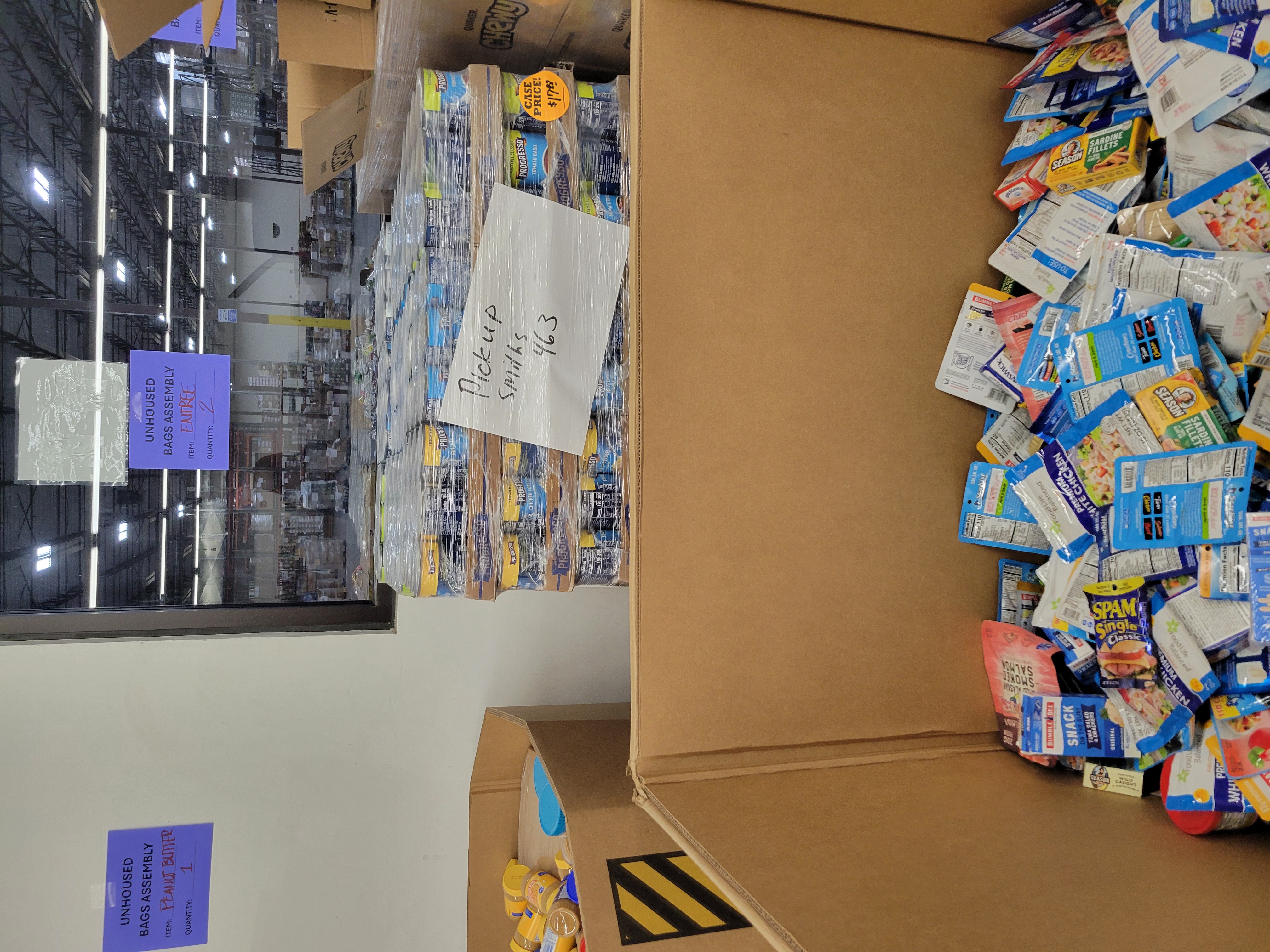 Cardboard containers and shelves of food for unhoused bag assembly line.
